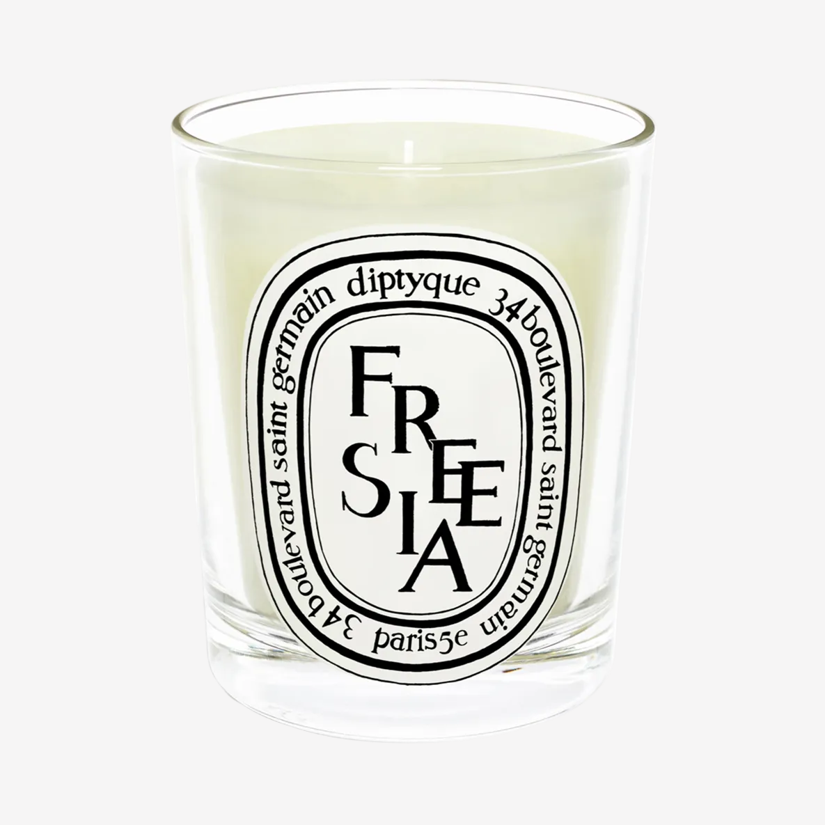 A clear glass candle with a white label that reads 'FREESIA' and the Diptyque logo.