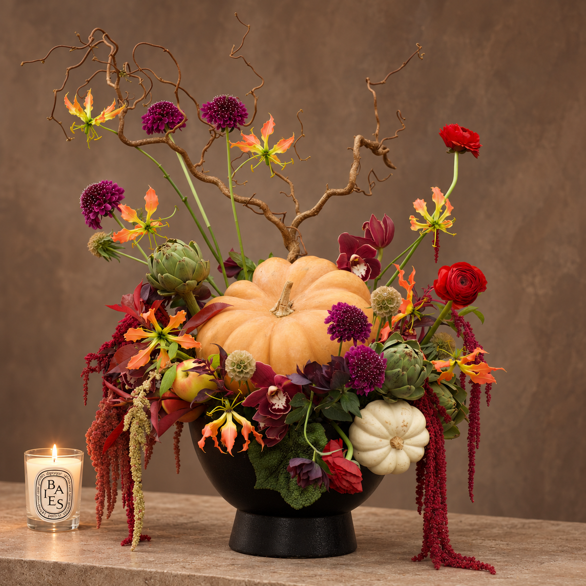 Pumpkin in Wonderland arrangement of Cymbidium orchids, gloriosa lilies, scabiosa, and pumpkins in a matte black cauldron